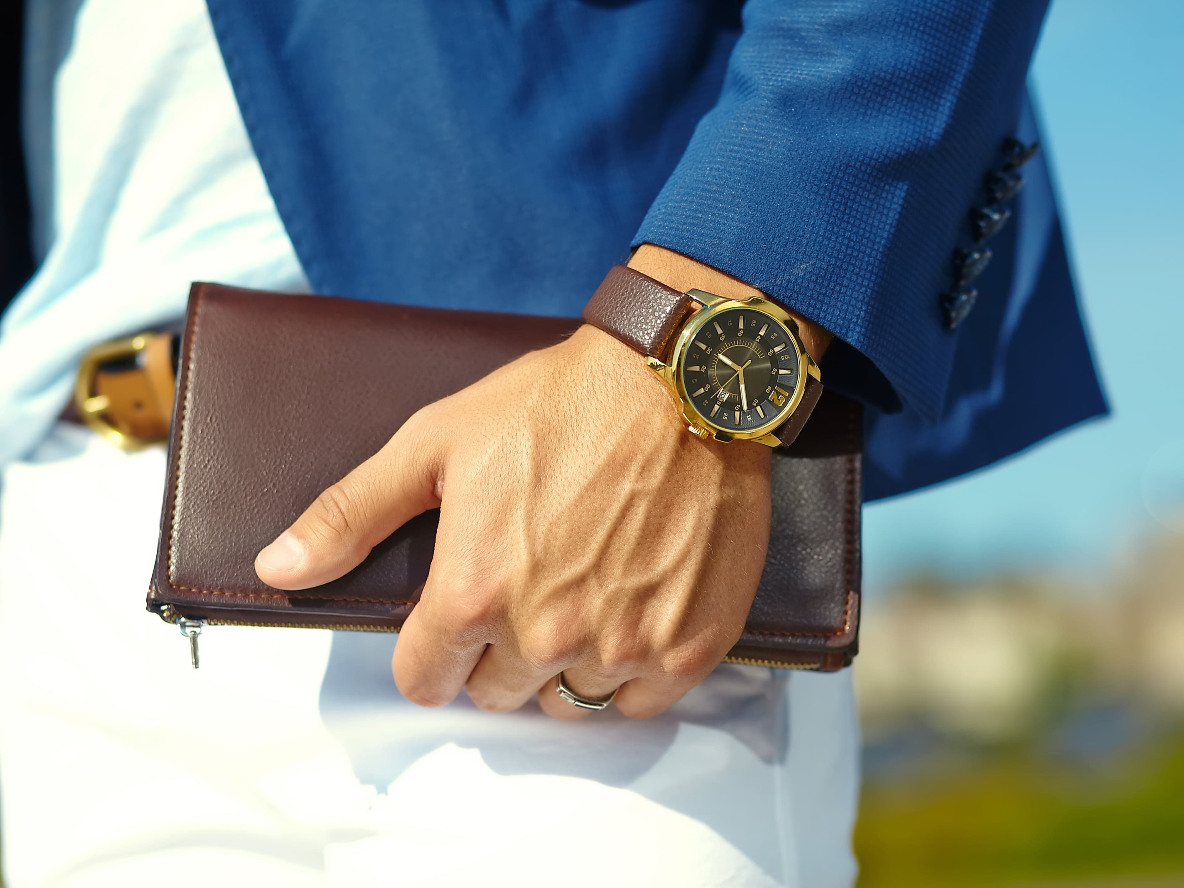 Hochwertige Vistora Seiko-Mod Herrenuhr mit goldfarbenem Gehäuse und schwarzem Zifferblatt, kombiniert mit einem braunem Lederarmband. Perfekt für stilbewusste Uhrenliebhaber. Getragen von einem Mann mit gepflegten Händen, einem blauen Anzug und weißer Hose sowie Hemd.